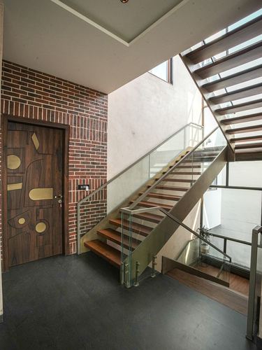 Double-height foyer with brick wall, brass-inlaid wooden door, and floating staircase with glass railing