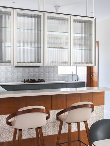 Kitchen with fluted glass cabinets, patterned tile backsplash, and wooden curved bar stools at island