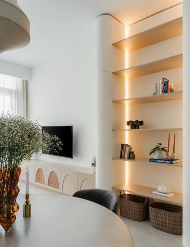 Living space with curved column, backlit wood shelving, arched cane TV console, and dining table in foreground