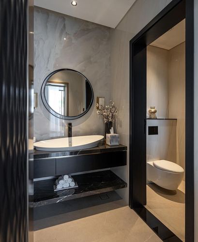 Dark marble bathroom vanity with round mirror and glimpse into black-framed toilet nook beyond