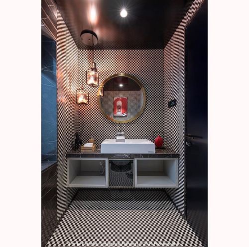 Powder room fully wrapped in black and white checkerboard tile with round gold mirror and floating vanity