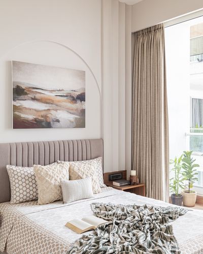 Beige bedroom with arched niche painting, tufted headboard, and sheer-curtained window with plants