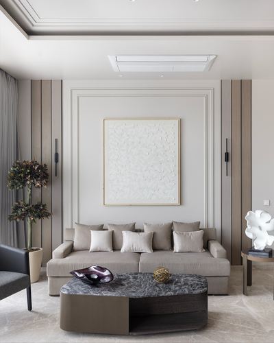 Neutral toned living room with paneled wall, textured art above beige sofa and oval marble coffee table