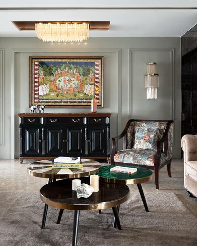 Living room with pichwai painting over black carved sideboard, patterned armchair, and round nesting coffee tables