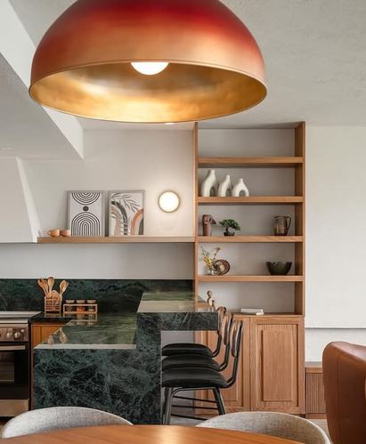 Kitchen with green marble waterfall island, wood open shelving, and large red-gold dome pendant light