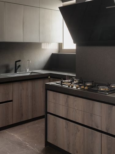 Modern kitchen with wood-toned cabinetry, dark stone counters, and angled black chimney hood over island hob.