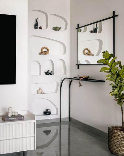 White foyer wall with sculpted niches, black mirror, console table and potted fig plant