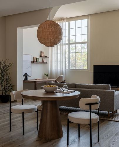 Japandi dining and living space with round wood table, boucle chairs, rattan pendant, and sofa near window