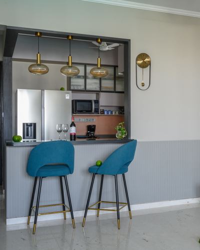 Teal bar stools face a kitchen pass-through with amber pendant lights and a brass pendulum clock