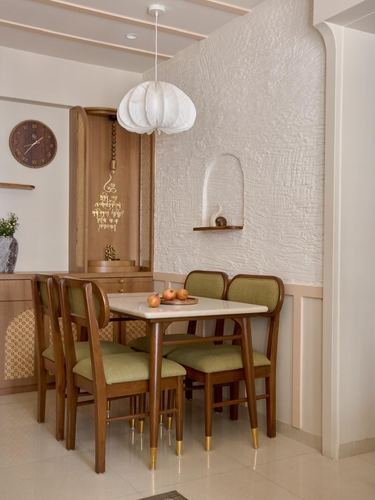 Wooden dining table with olive chairs beside a textured plaster wall with arched niche and pendant lamp