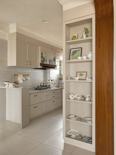 Beige kitchen seen through arched opening beside a shelving alcove filled with crockery