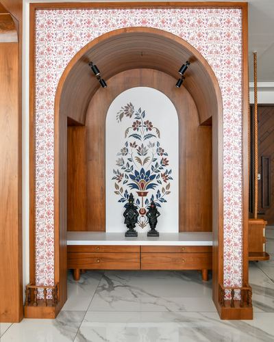 Arched wooden pooja niche with floral mural and two brass idols on marble ledge