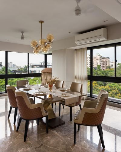 Dining room with glass table, amber bubble chandelier, and floor-to-ceiling windows overlooking green Kolkata skyline