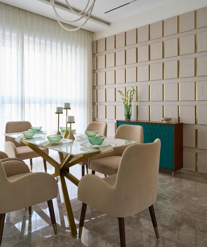 Dining room with glass-top brass table, beige velvet chairs, and gold-veined paneled wall