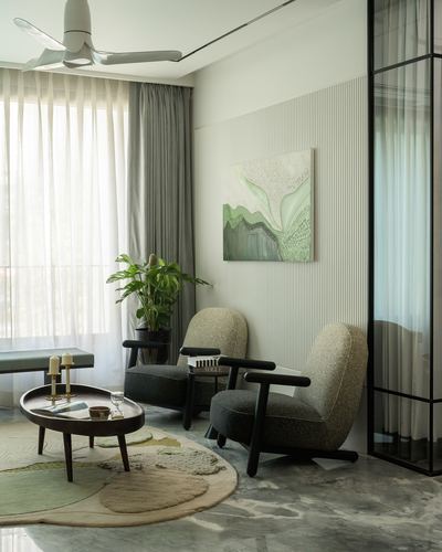 Living room corner with two dark-armed armchairs, round wood table, green abstract art on fluted wall