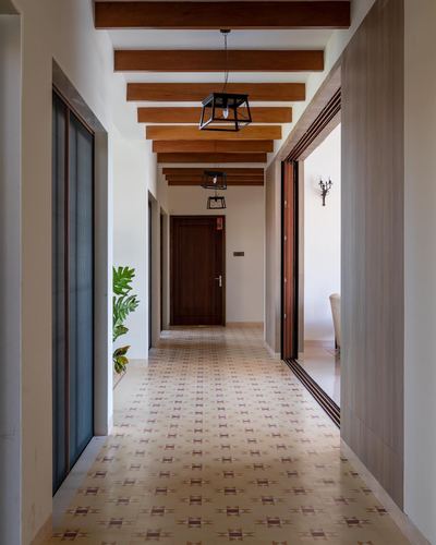 Long corridor with wooden beam ceiling, patterned tile floor, hanging lanterns and a wooden door at the end