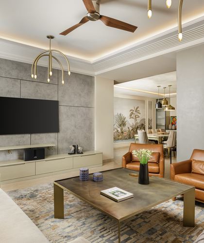 Living room with stone TV wall, tan leather armchairs, brass chandelier and dining area beyond