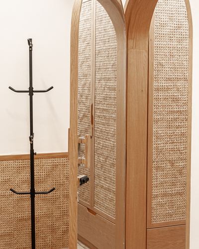 Arched cane-paneled oak wardrobe beside a black coat stand and cane wainscoted wall