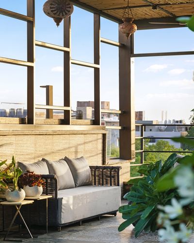 Rooftop terrace lounge with wicker sofa, hanging lanterns, and steel-framed glass walls overlooking city skyline