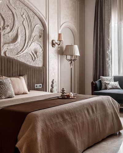 Bedroom with carved relief headboard panel, pleated velvet bed base, arched niche and brass floor lamp beside a grey sofa