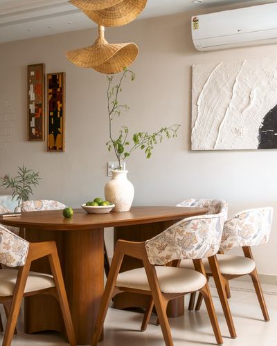 Wooden oval dining table with floral chairs under woven rattan pendant lights and textured wall art