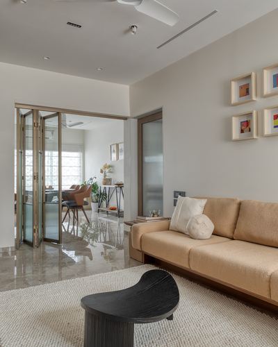 Living room with tan sofa, black sculptural coffee table, marble floor, and folding glass doors to dining area