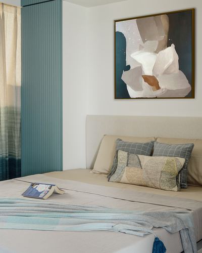 Neutral bedroom with beige upholstered headboard, patterned pillows, and abstract painting above