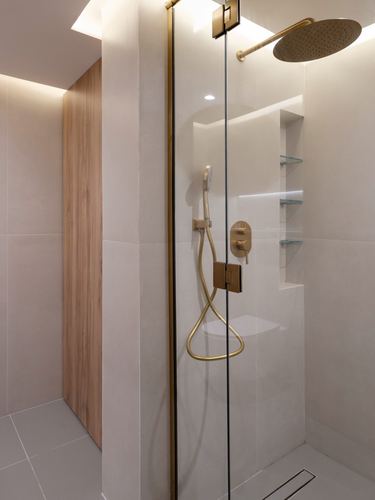 Walk-in shower with brass fixtures, glass partition, and wood-clad wall niche