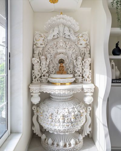 Ornately carved white marble temple niche with a small gold idol beside a window