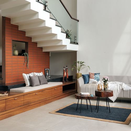 Living room with terracotta brick staircase wall, built-in wood bench, and beige sofa with layered rugs