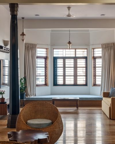 Living room with wooden floor, bay window seating, cane chair, and hanging lanterns in daylight
