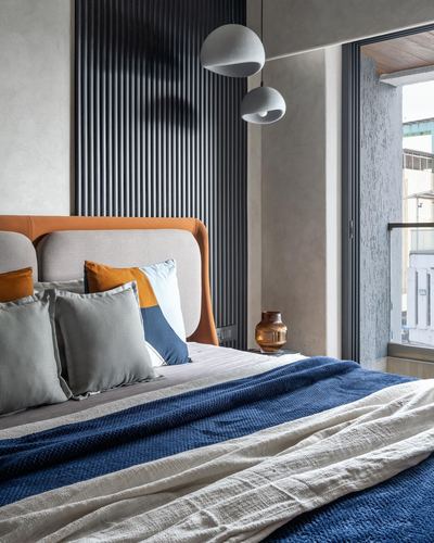 Bedroom with orange leather-trimmed headboard, blue and cream bedding, two globe pendant lights, textured wall