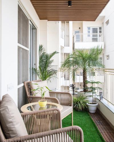 Small apartment balcony with rattan chairs, glass table, turf flooring, and potted palms against city view