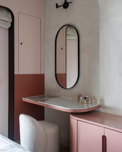 Pink and terracotta bedroom corner with oval mirror, marble vanity ledge and boucle stool