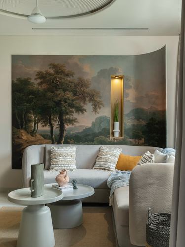Living room corner with beige sofa, mustard cushion, and large painted landscape mural with lit niche