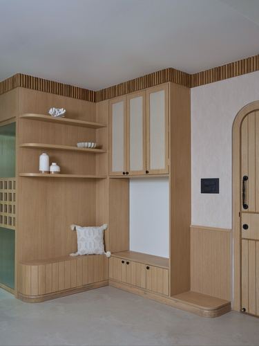 Wooden foyer built-in with open shelving, cabinetry, bench, and arched door in beige tones