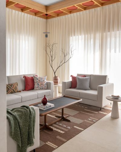 Cream sofas around a wood coffee table beneath a terracotta-coffered ceiling and sheer curtains