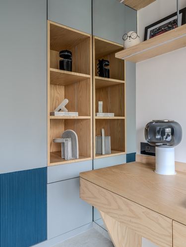 Built-in plywood shelving with ceramic and wood sculptures beside a wooden desk with glass lamp