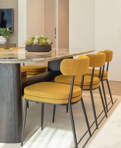 Close view of dining table with marble top, dark pedestal base, and mustard upholstered chairs on black metal legs