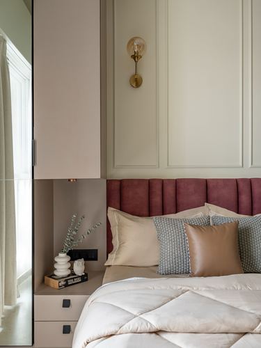 Bedroom corner with maroon tufted headboard, brass sconce, panelled wall, and layered pillows