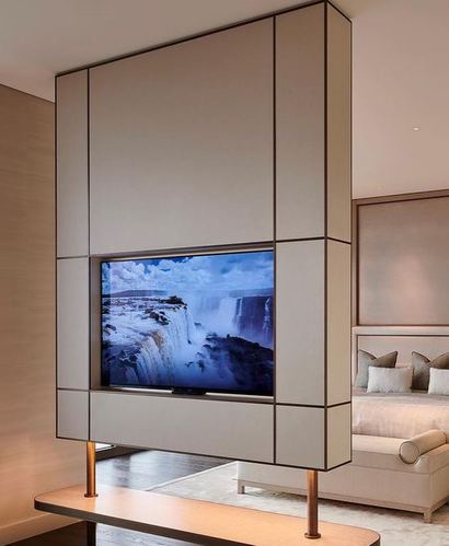 Floating paneled TV cabinet on brass legs dividing a neutral-toned bedroom with upholstered headboard