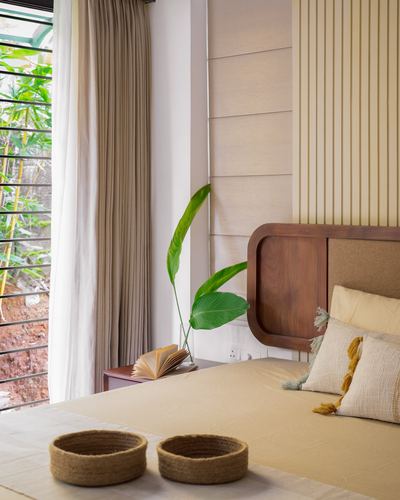 Bedroom corner with wood-framed headboard, ribbed wall panels, and a garden view through curtained window