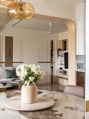 Marble dining table with flower vase framed by curved wooden archway leading to living room