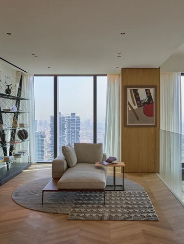 Minimalist living room with chaise lounge, layered rugs, oak paneling and city skyline view