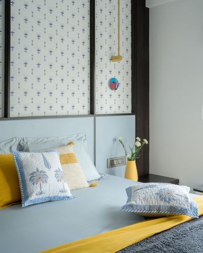 Bedroom with blue and mustard bedding against floral wallpaper panels and dark wood headboard.