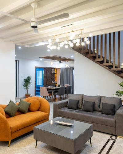 Living room with grey and orange sofas, glass coffee table, and open wooden staircase behind