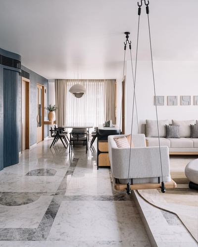 Living and dining area with patterned marble floor, hanging swing chair, sofa, and dining table beyond