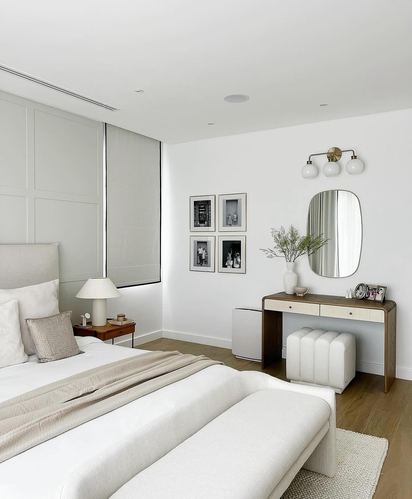 Neutral bedroom with paneled headboard, gallery wall, and wood vanity under an oval mirror