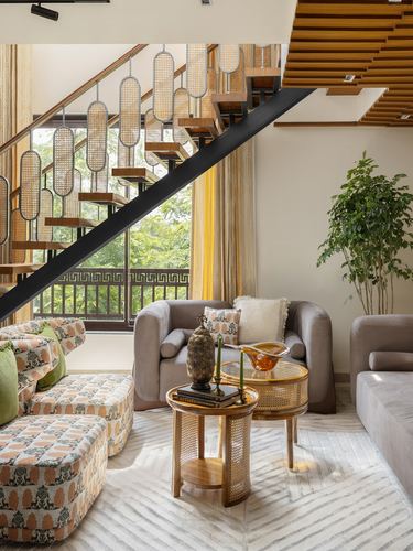 Living room beneath a staircase with cane pendant lights, grey armchairs, and a cane side table