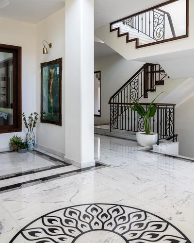 Marble foyer with inlaid floor medallion, scrolled iron staircase, and framed painting under a sconce
